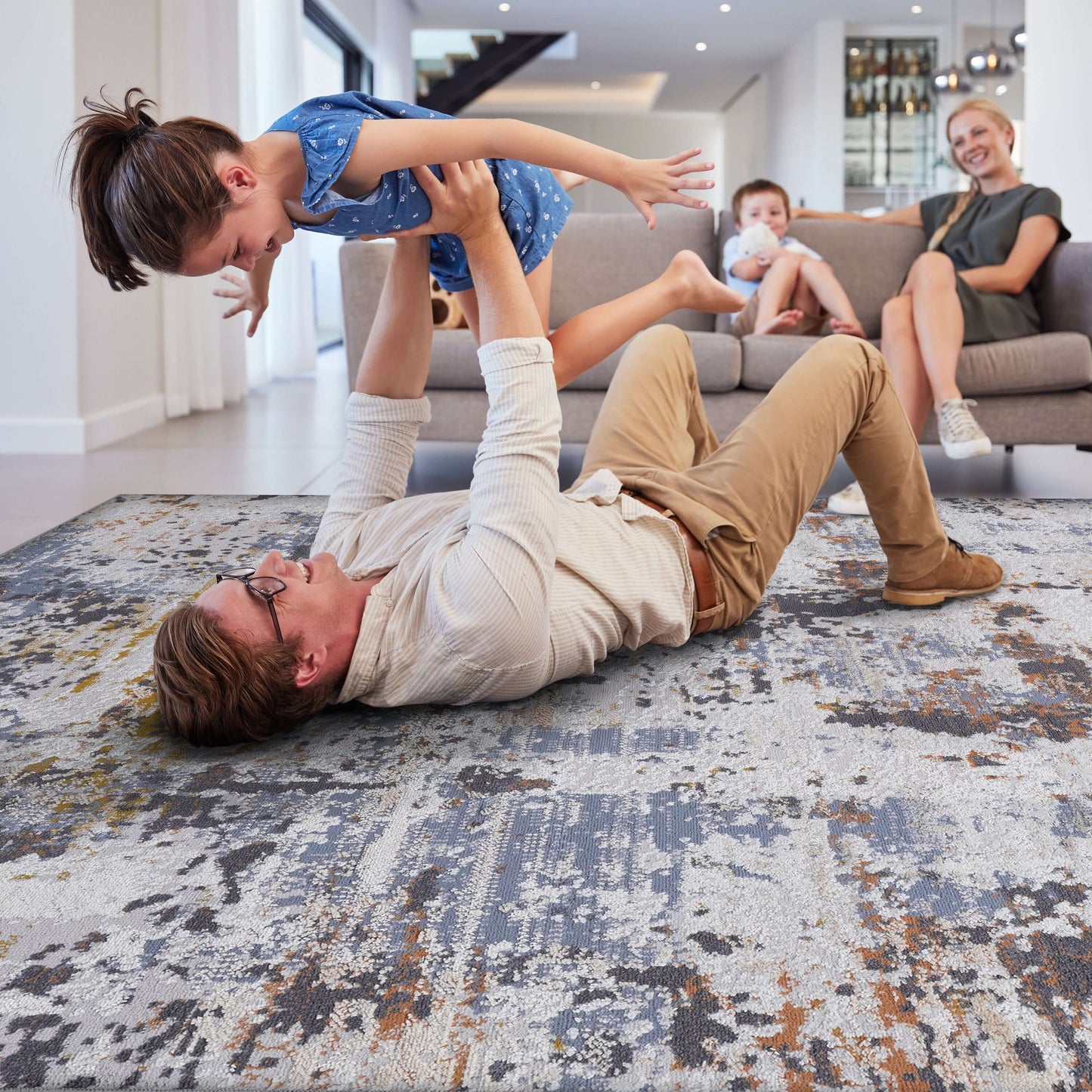 A father playing joyfully with his daughter on a Multicolor Abstract Area Accent Rug in a modern living room.