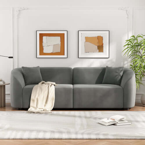 Contemporary sloped arm boucle upholstered sofa in grey, featuring bold curves and luxurious comfort against modern artwork.