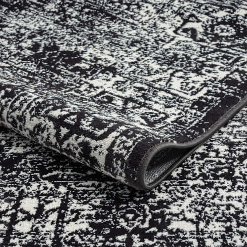 Distressed vintage Persian styled woven area rug with intricate patterns in black and white, ideal for modern decor.