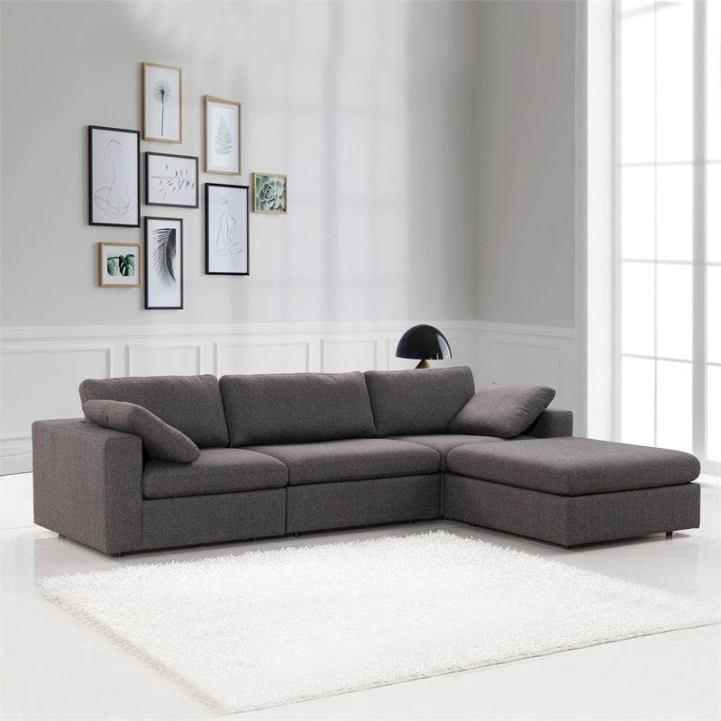 A bright living room with large windows features the Ashcroft Furniture Cecilia Dark Gray Modular Chaise Sofa Sectional 121, a reversible chaise, white shag rug, black table lamp on a side table, and a gallery wall of framed art against white walls.