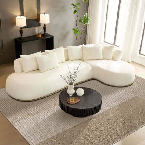 Rounded L-Shaped chaise sofa sectional in cream with decorative pillows and modern coffee table in stylish living room.