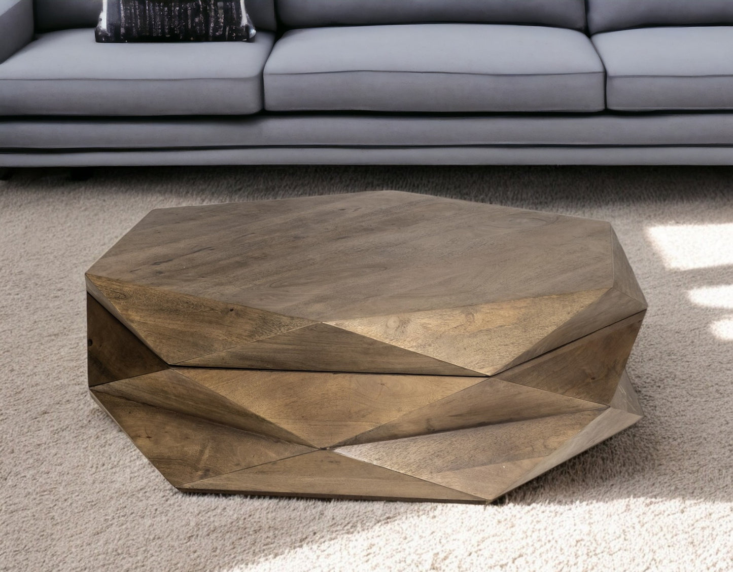 The Home Roots Hexagonal Solid Wood Coffee Table With Storage 48 adds geometric elegance to any space, its faceted design casting striking shadows on a light carpet in front of a gray sofa.