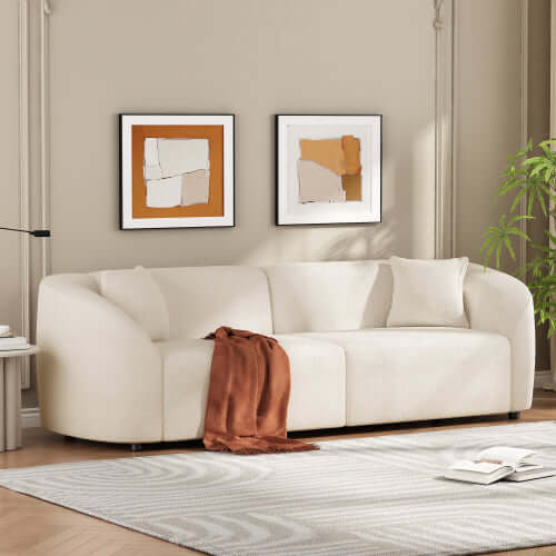 Contemporary sloped arm boucle upholstered sofa in cream color, accented with cozy throw and modern wall art.