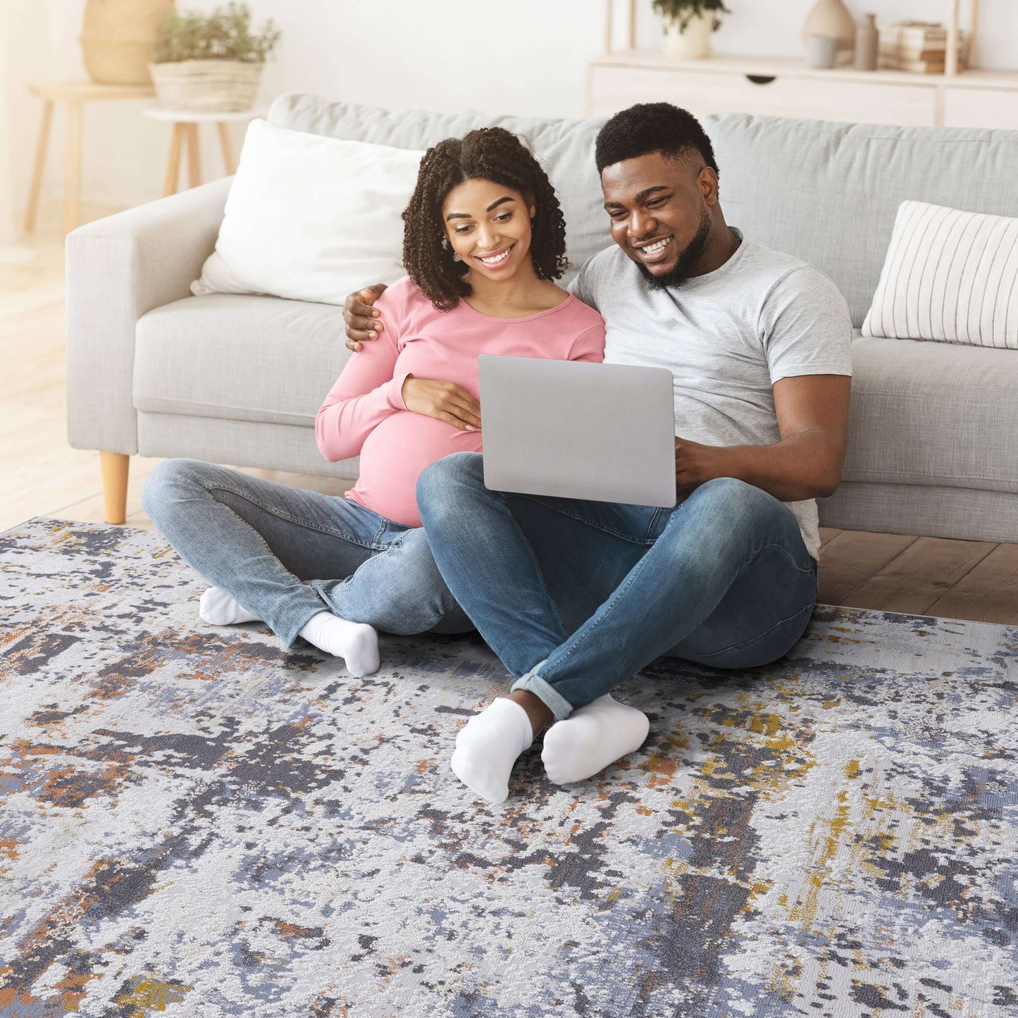 Couple sitting on a multicolor abstract area rug, enjoying time together with a laptop in a cozy living room.