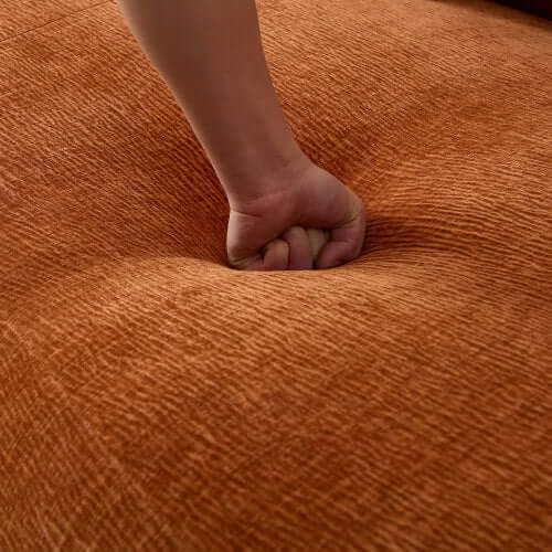 Hand pressing down on the soft, textured fabric of an orange chaise sofa cushion.