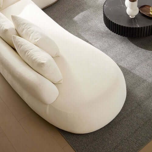 Cream rounded L-shaped chaise sofa sectional with plush pillows on a stylish rug.