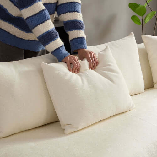 Person adjusting soft cream pillows on a cozy rounded L-shaped chaise sofa sectional.
