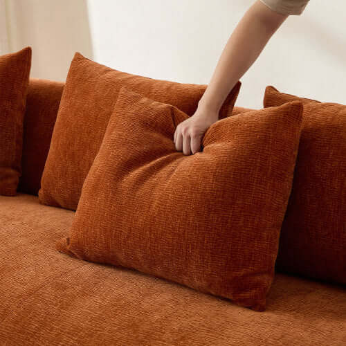 Close-up of hand adjusting plush orange sofa pillows on a cozy sectional couch.