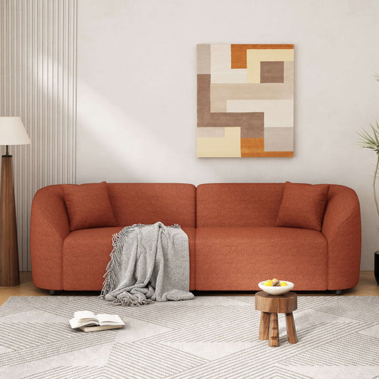 Contemporary sloped arm boucle sofa in warm orange color, featuring a cozy throw blanket, set in a stylish living space.