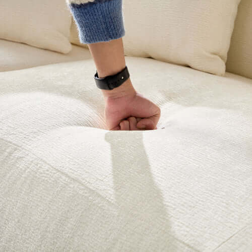 Hand pressing into the plush surface of a cream-colored chaise sofa, showcasing its comfort and softness.