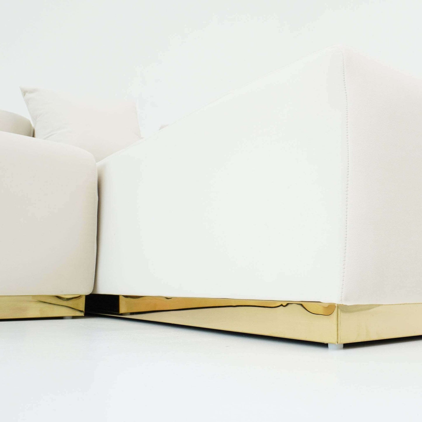 Close-up view of a modern white sofa with a luxurious gold base, showcasing elegant design and plush upholstery.