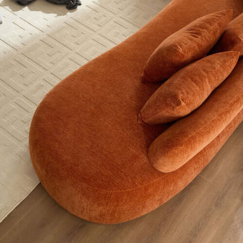 Close-up of an orange rounded L-shaped chaise sofa with plush pillows, showcasing modern design and comfort.