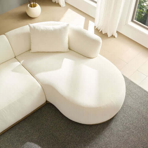 Top view of a rounded L-shaped chaise sofa sectional in cream color, featuring a plush armrest and decorative pillow.
