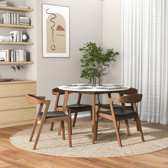 A modern dining area features the Ashcroft Furniture Alina MCM Round Walnut Wood Dining Table 43, four wooden chairs with black cushions, a green plant centerpiece, beige rug, light wood floors, dresser, shelves with decor, and abstract wall art.