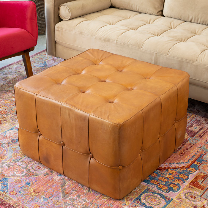The Benjiro Button Tufted Square Leather Ottoman 27 by Ashcroft Furniture Co adds mid-century modern charm, sitting on a colorful rug between a red chair and beige sofa in this cozy living room.