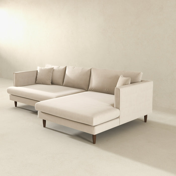 The Blake Velvet Upholstered L-Shape Chaise Sofa Sectional 107 by Ashcroft Furniture, featuring plush velvet and reversible chaise design on wooden legs, adds modern style to a minimalistic room with light walls and floors.