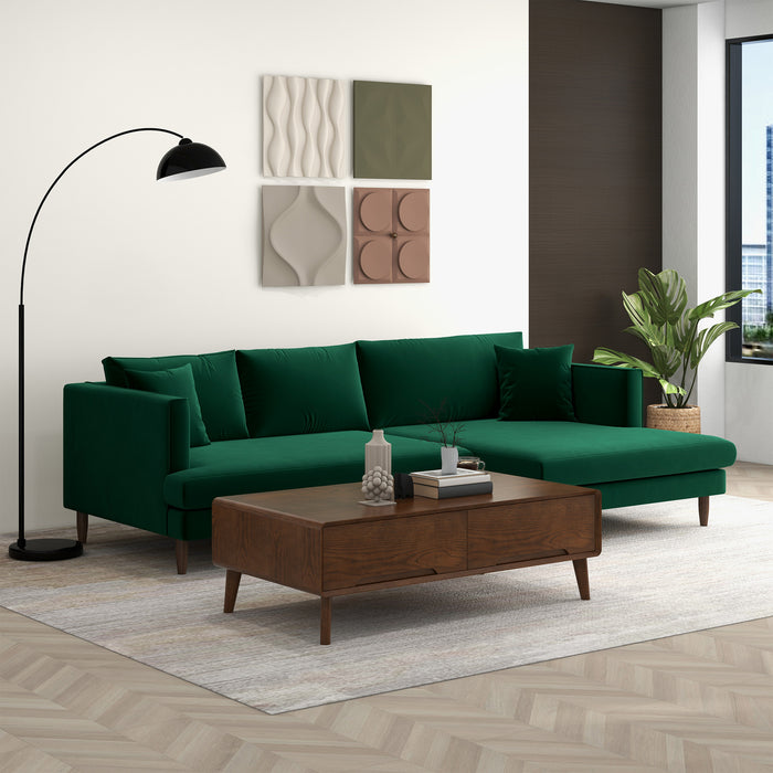 A modern living room with the Ashcroft Furniture Blake Velvet Upholstered L-Shape Chaise Sofa Sectional 107 in green, a dark wood coffee table, floor lamp, potted plant, four abstract wall art pieces, light area rug, and herringbone wood floor.
