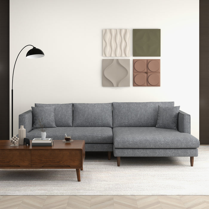 A modern living room features the Blake Velvet Upholstered L-Shape Chaise Sofa Sectional 107 by Ashcroft Furniture, a wooden coffee table with books and decor, a black floor lamp, light rug, and four geometric wall art pieces.