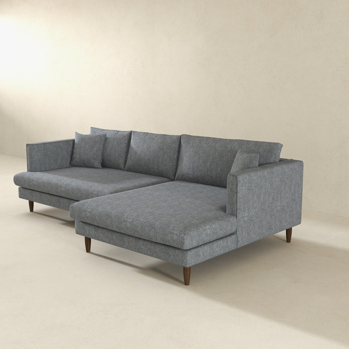 The Ashcroft Furniture Blake 107 Velvet Upholstered L-Shape Chaise Sofa Sectional, in modern gray with wooden legs and plush cushions, features a left-side reversible chaise, set against an off-white wall and floor.