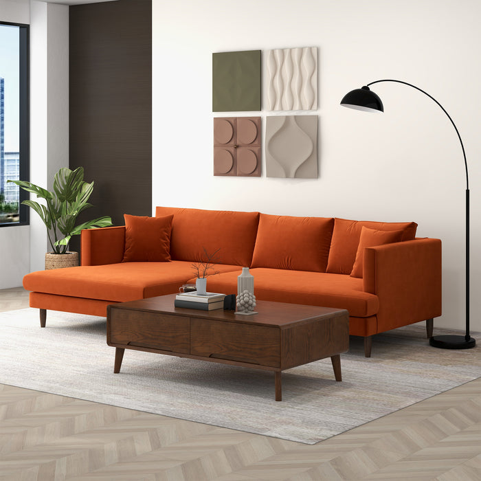 A modern living room features the Ashcroft Furniture Blake Velvet Upholstered L-Shape Chaise Sofa Sectional 107 in orange, a wooden coffee table, black arc floor lamp, textured wall art, a potted plant by the window, and a light rug on wooden floors.