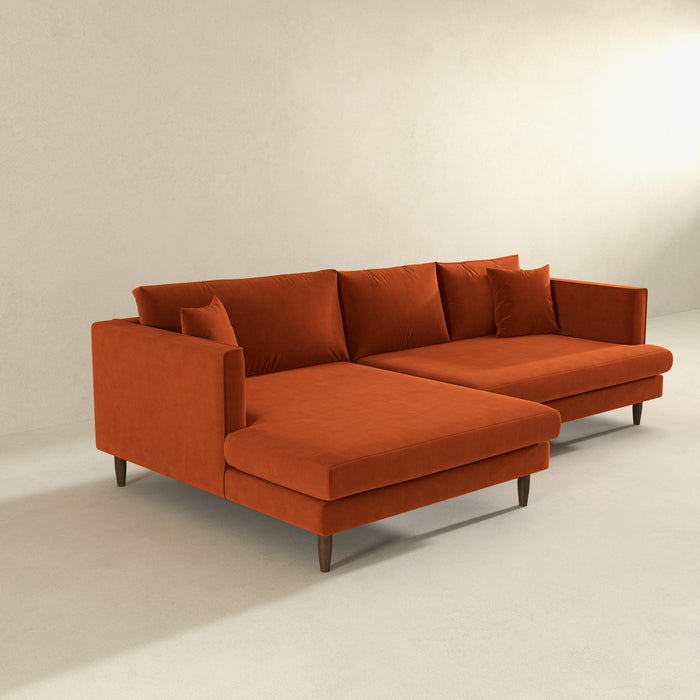 The Ashcroft Furniture Blake Velvet Upholstered L-Shape Chaise Sofa Sectional 107 features plush burnt orange velvet, clean lines, matching cushions, wooden legs, and a reversible chaise, perfect for minimalist rooms with light walls and floors.