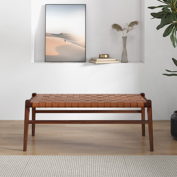 The Cody MCM Strapped Genuine Leather Bench 44 by Ashcroft Furniture sits on a light wood floor in a minimalist room, with a shelf holding décor and a leafy plant in the corner.