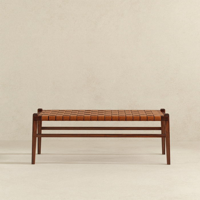 The Ashcroft Furniture Cody MCM Strapped Genuine Leather Bench 44 features a tan leather woven seat and minimalist mid-century modern wooden design, shown against a plain light-colored wall and floor.