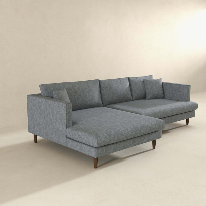 The Blake Velvet Upholstered L-Shape Chaise Sofa Sectional 107 by Ashcroft Furniture features plush velvet upholstery, wooden legs, and a reversible chaise for comfort and flexibility in a minimalist room with light walls and flooring.