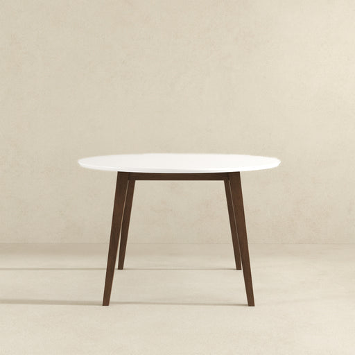 The Alina MCM Round Walnut Wood Dining Table 43 by Ashcroft Furniture, with a white top and four angled dark walnut legs, stands on a light beige floor against a neutral, light-colored wall.