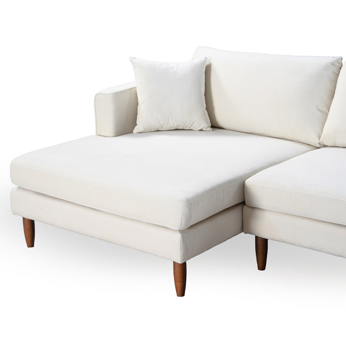 The Ashcroft Furniture Blake Velvet Upholstered L-Shape Chaise Sofa Sectional 107 features plush velvet upholstery, wooden legs, a left-facing chaise lounge, and comes with a matching white cushion for added comfort.