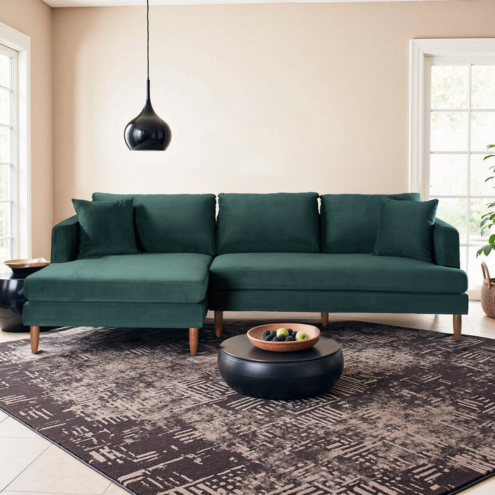 A modern living room with the Blake Velvet Upholstered L-Shape Chaise Sofa Sectional 107 by Ashcroft Furniture, a black round coffee table with fruit bowl, patterned rug, black pendant light, and large windows letting in natural light.