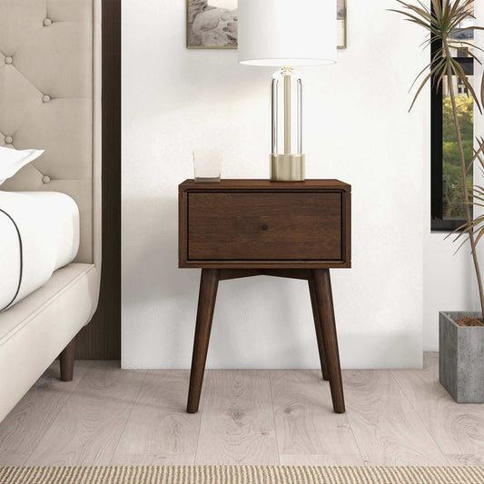 The Avery Solid Wood Nightstand with Drawer by Ashcroft Furniture Co. features a walnut finish, mid-century modern design, single drawer, and tapered legs. Its styled beside a beige bed with a glass lamp, water glass, wall art, window, and nearby plant.