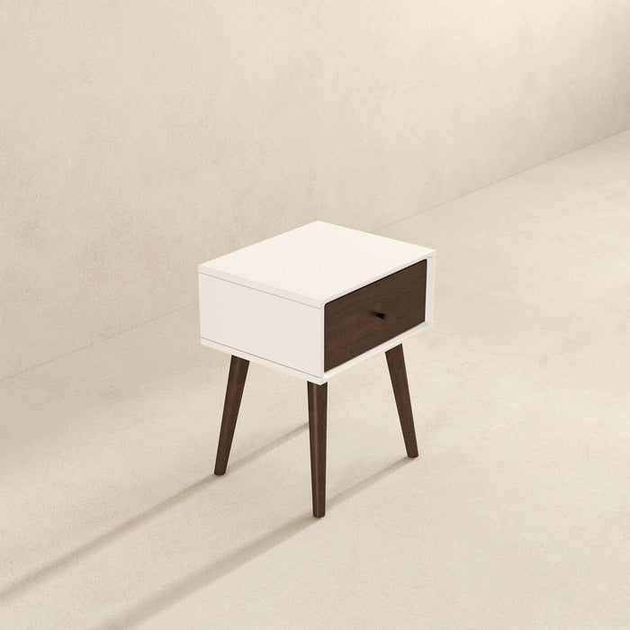 The Avery Solid Wood Nightstand with Drawer by Ashcroft Furniture Co. showcases a white rectangular body, single walnut-finished drawer, and four angled dark brown legs, standing on a light floor against a beige wall.