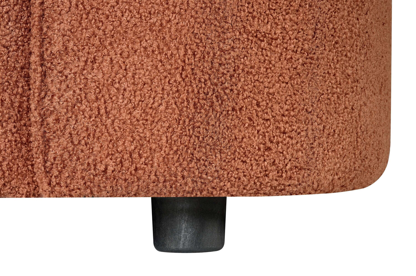 Close-up of the soft bouclé upholstery and black leg of a contemporary sofa in warm rust color.