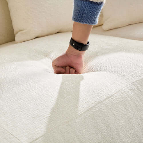 Close-up of a hand pressing down on the plush fabric of a cream sectional sofa, showcasing its comfort and softness.