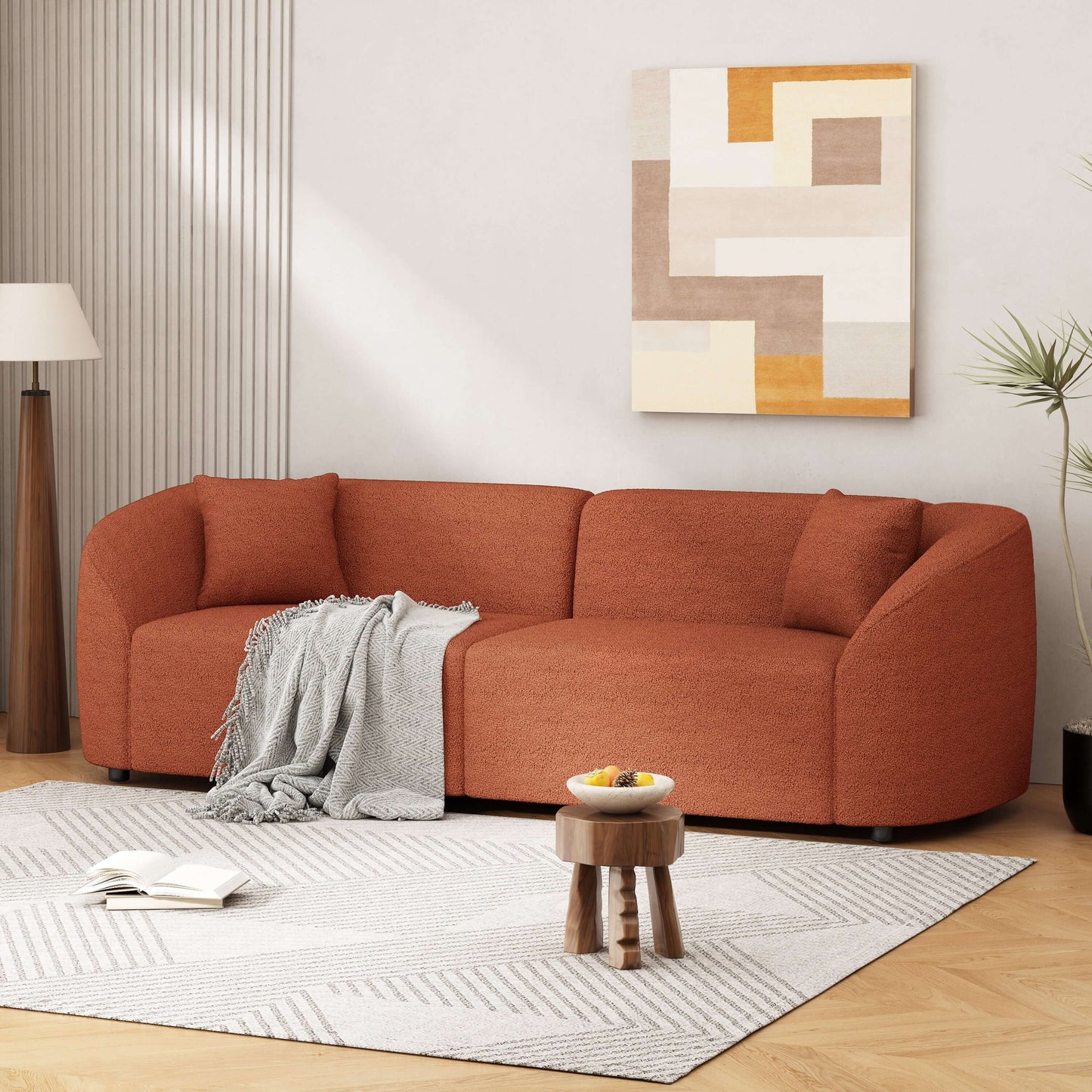 Contemporary sloped arm boucle upholstered sofa in warm orange, featuring curved design and cozy throw blanket.