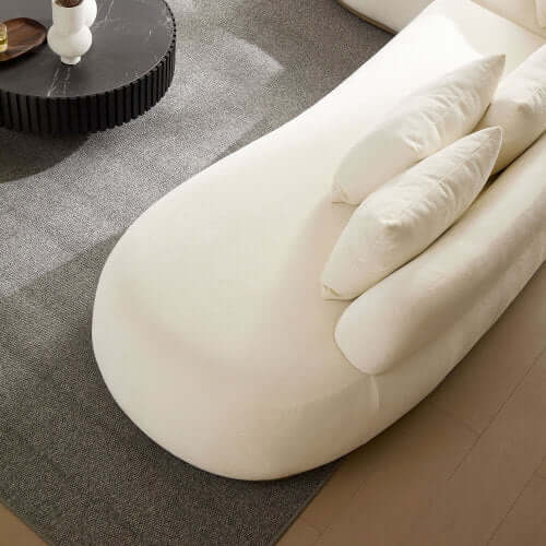 Cream rounded L-shaped chaise sofa with plush pillows, showcased in a modern living room setting.