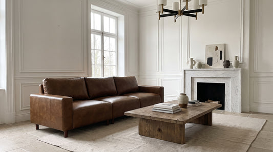 Brown leather sofa in a bright paneled living room with a marble fireplace, showing the soft sheen and grain of a well-maintained leather sofa.