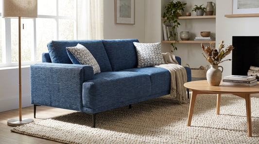 Blue chenille upholstered sofa in a bright Scandinavian living room, the woven fabric texture visible across the arm and seat cushions.