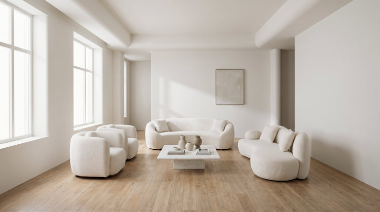An all-white minimalist living room with a curved boucle sofa and two matching armchairs, a marble coffee table, and abundant negative space