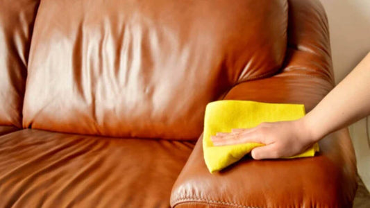 Person cleaning a leather sofa with a yellow cloth, showcasing upholstery care techniques.