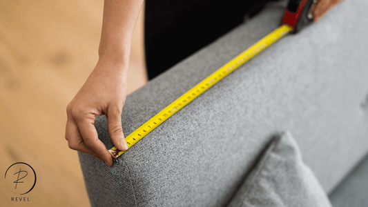 Person measuring a gray sofa with a tape measure for online furniture shopping.