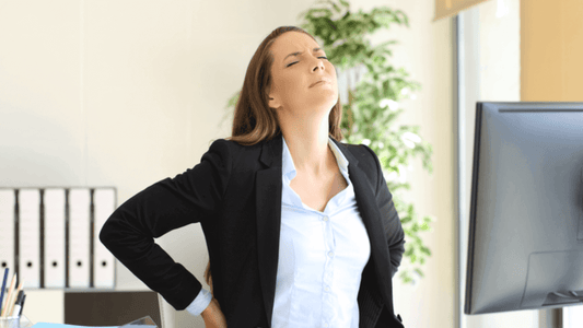 Woman with back pain in an office setting, highlighting the need for ergonomic furniture in home workspaces.