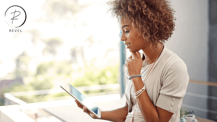 Woman with curly hair thoughtfully browsing on a tablet in a bright, modern setting.