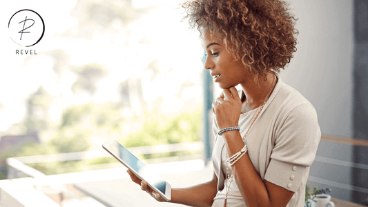 Woman with curly hair thoughtfully browsing on a tablet in a bright, modern setting.