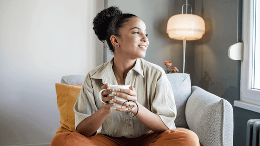 Smiling woman holding a mug in a cozy living room, enjoying a moment of relaxation and tranquility.