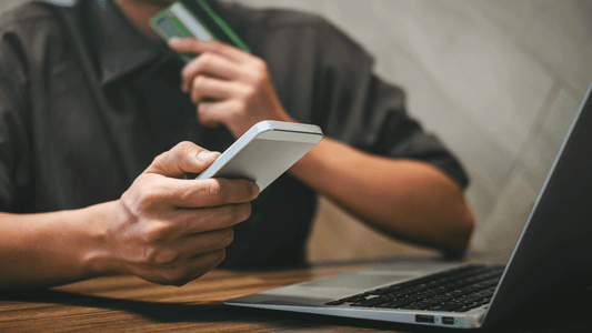 Person holding a smartphone and credit card while shopping online at a laptop.