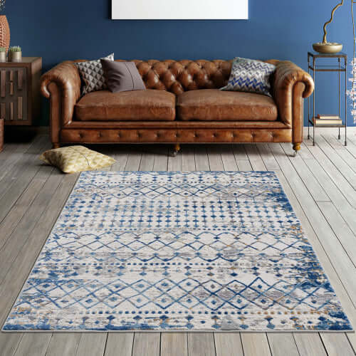 Moroccan styled blue and beige area rug on wooden floor in living room with brown leather sofa.