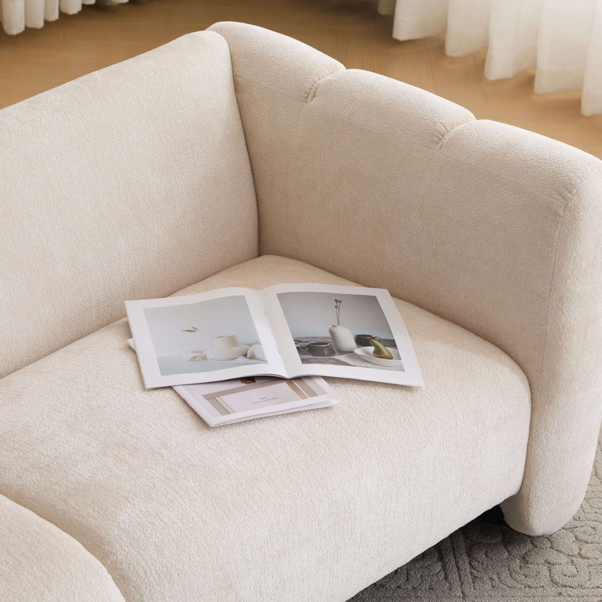 Tonson Boucle Sofa – 83” Curved Wave 3-Seater Sofa (3 Colors, Modern Sculptural Design) with magazines on it.