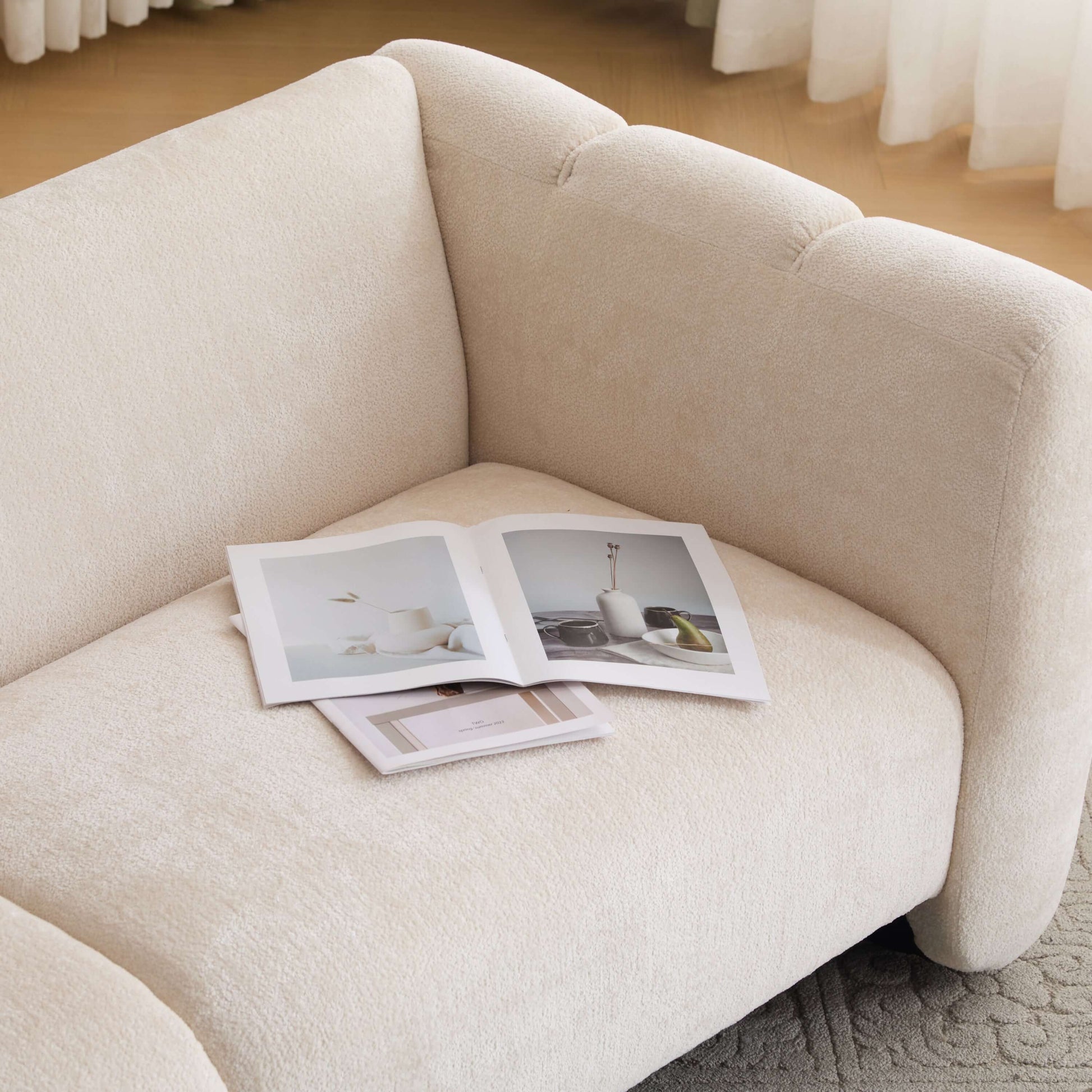 Tonson Boucle Sofa – 83” Curved Wave 3-Seater Sofa (3 Colors, Modern Sculptural Design) with magazines on it.